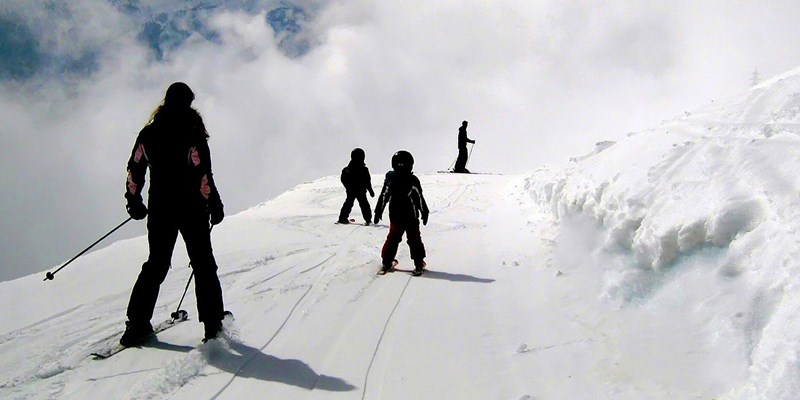 Parent skiing behind children on white snowy piste