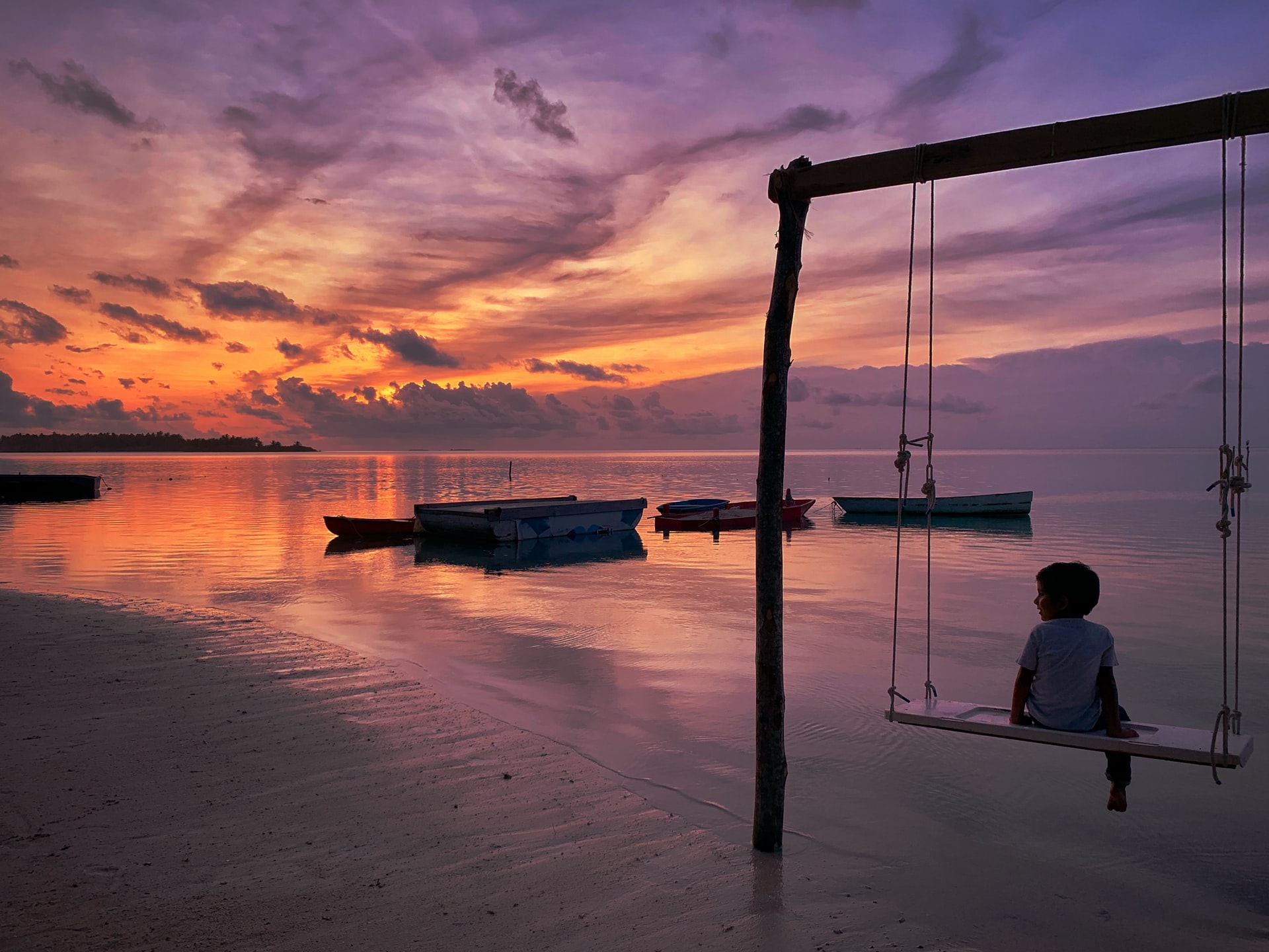 Little boy swinging on a beach swing in the sunset