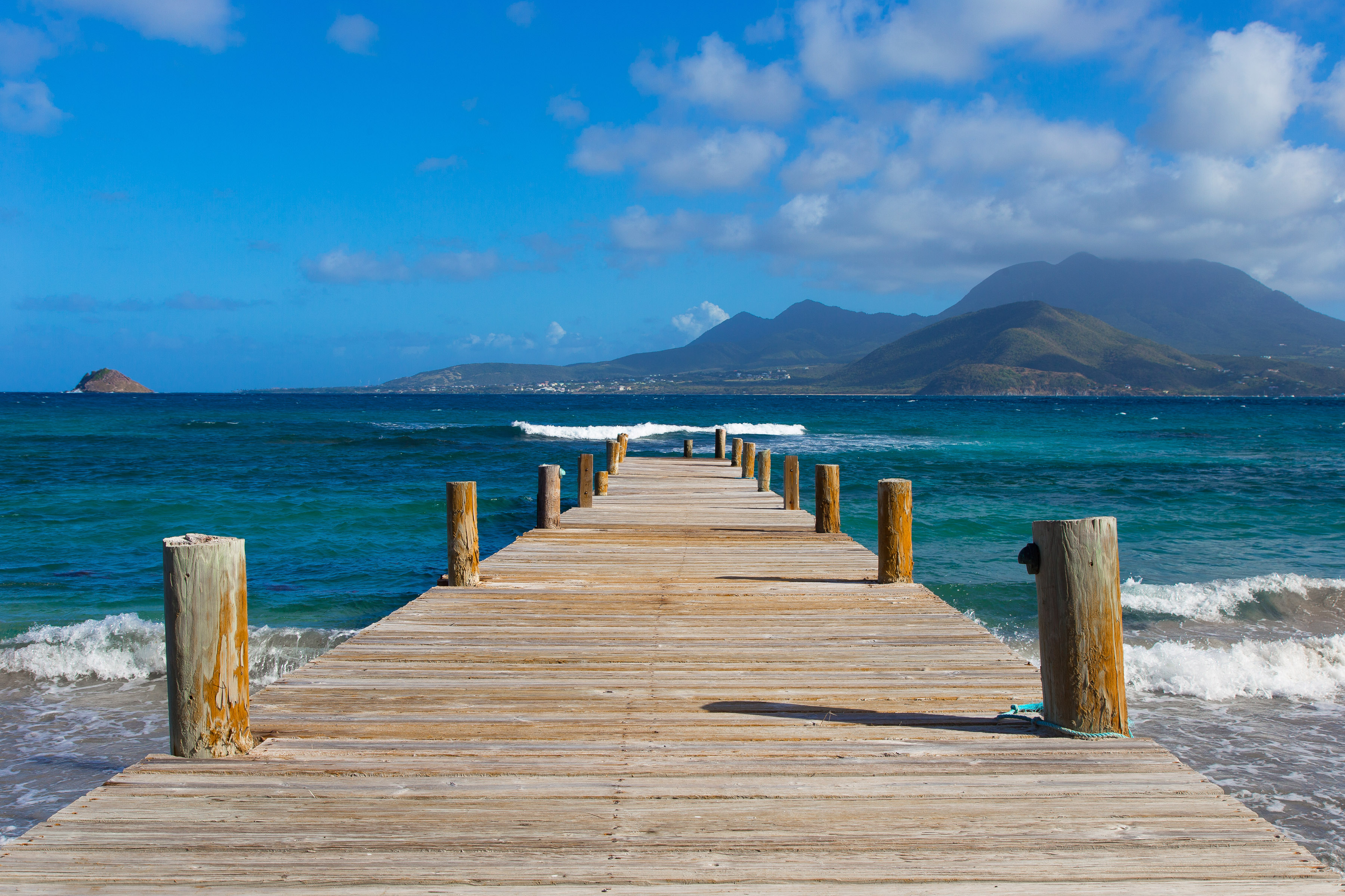 Pier over wavy bright blue sea with mountainous island in the distance