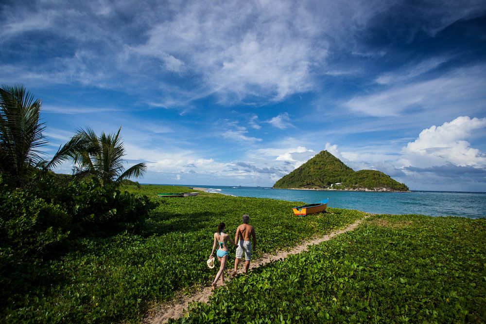 Couple walking along a small grassy path to a wild tropical beach