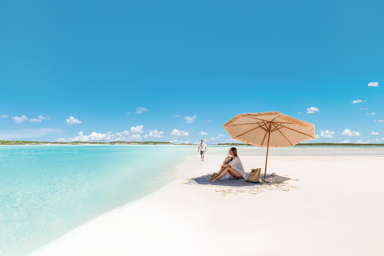 woman under parasol on sandy beach against turquoise Caribbean ocean & azure sky