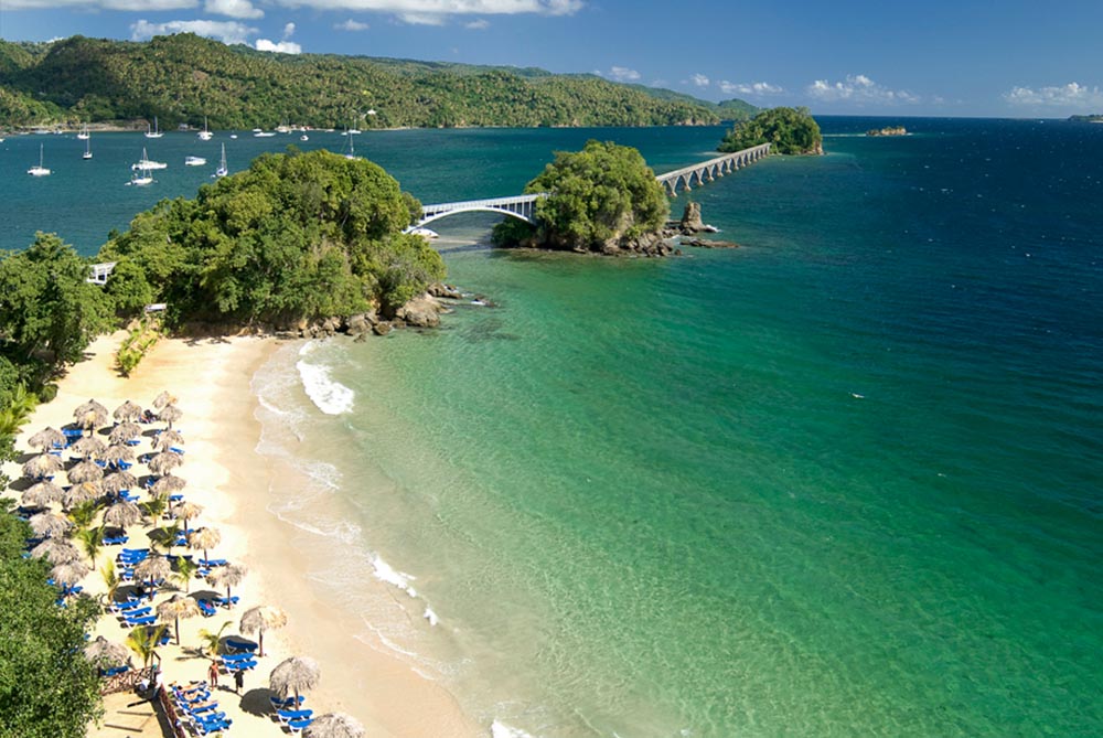 Sun beds and beach umbrellas lined up on a narrow tropical beach 