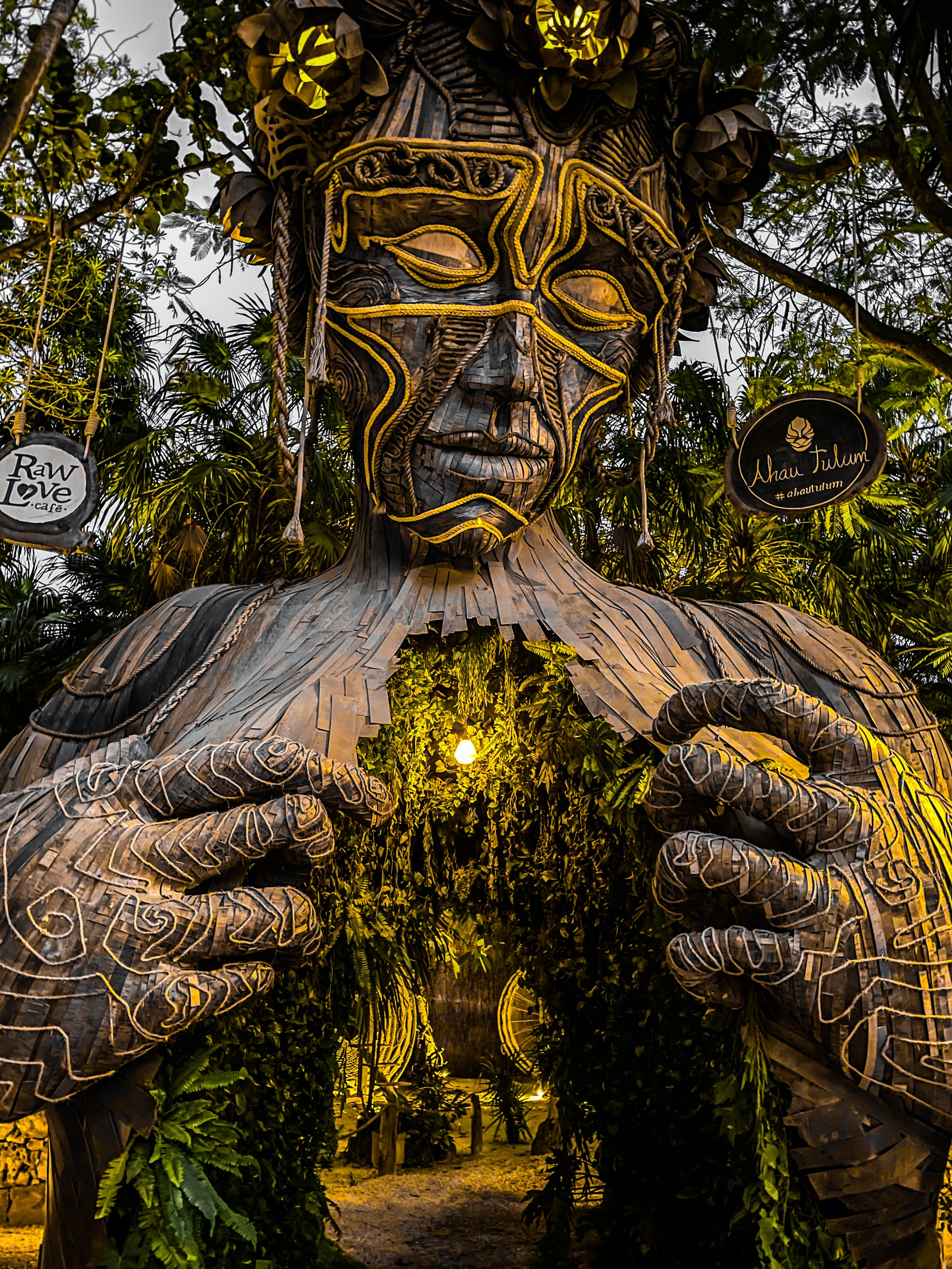 Towering wooden sculpture of a woman with tropical trees surrounding it 