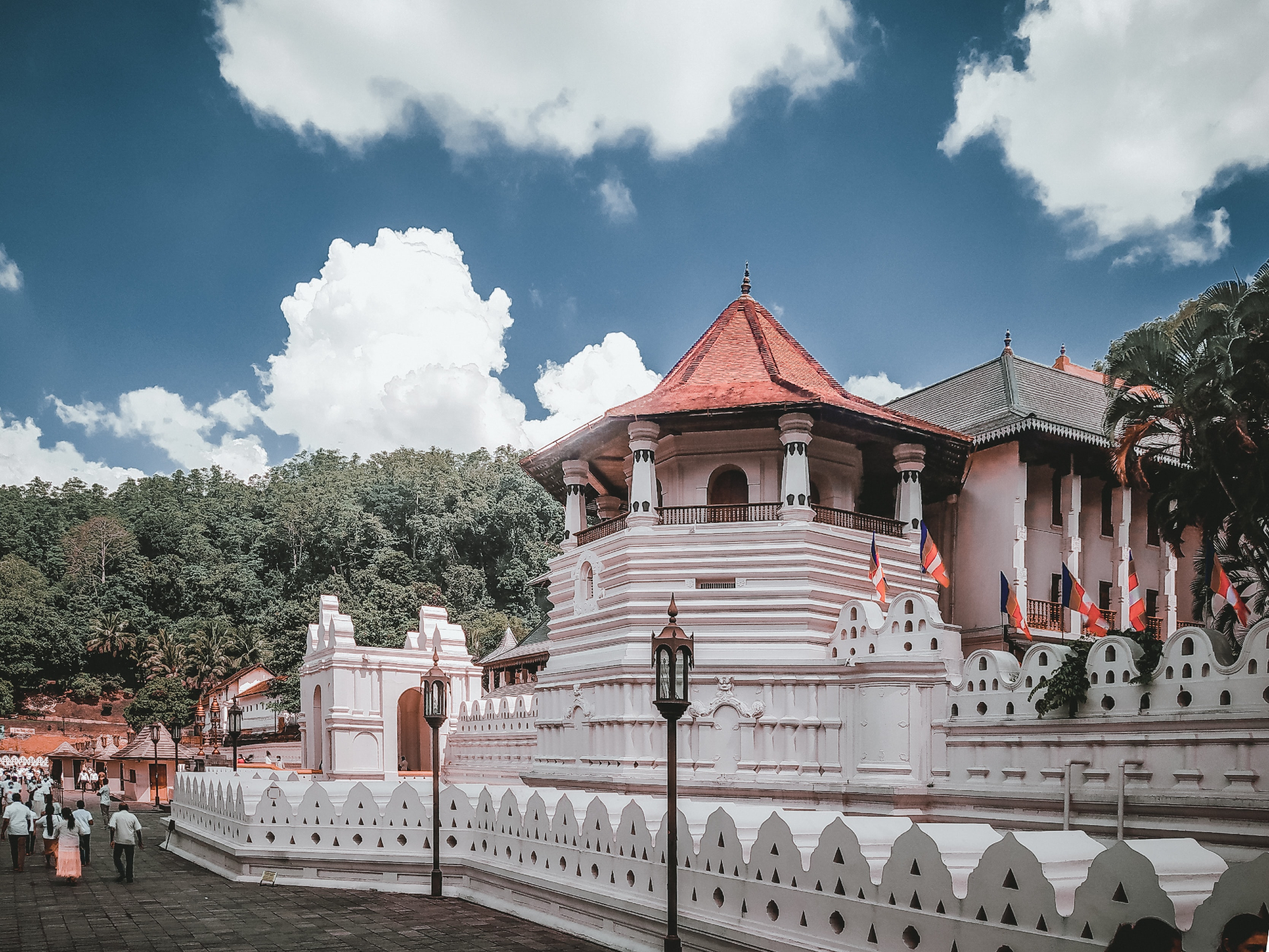White and red temple with large green trees and clouds in background 