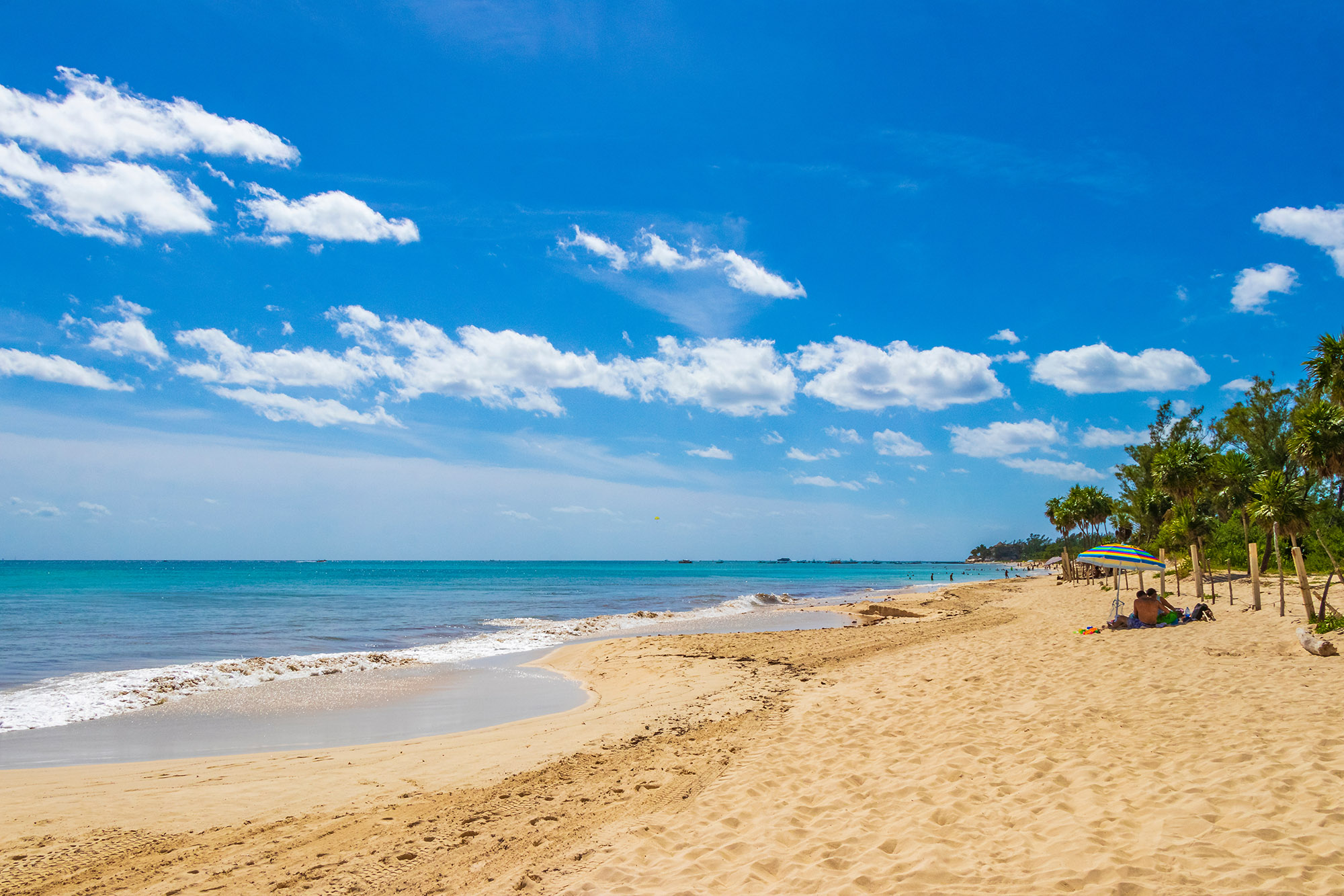 Two people sitting under a parasol on a golden sand tropical beach