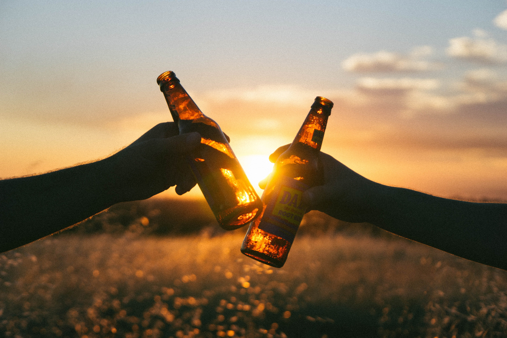 2 beer bottles knocking together with sunset shining through