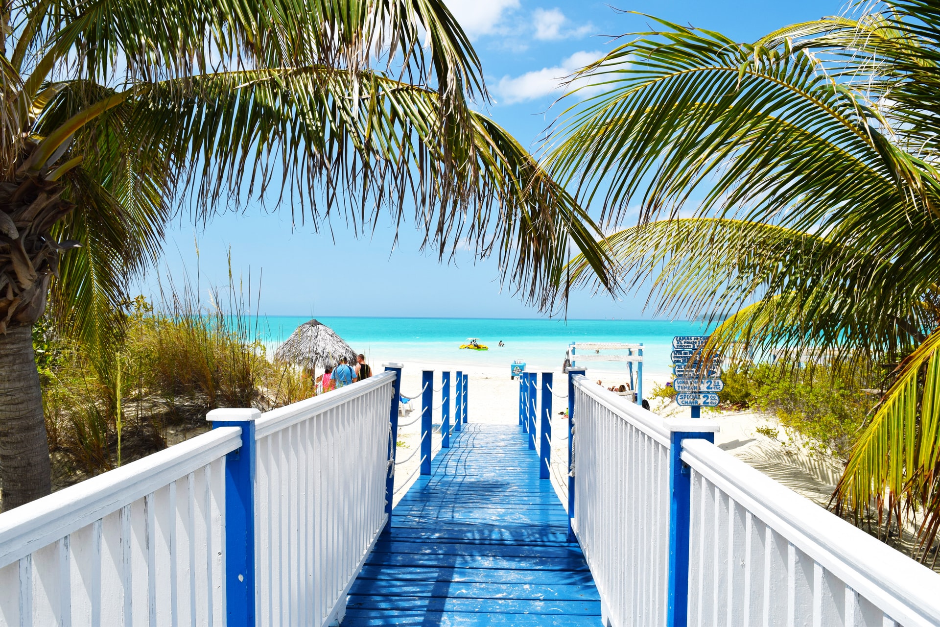 Blue and white bridge leading to a white sand tropical beach 
