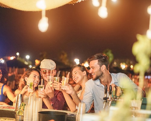 Happy friends cheering and drinking cocktails at the bar of a beach party