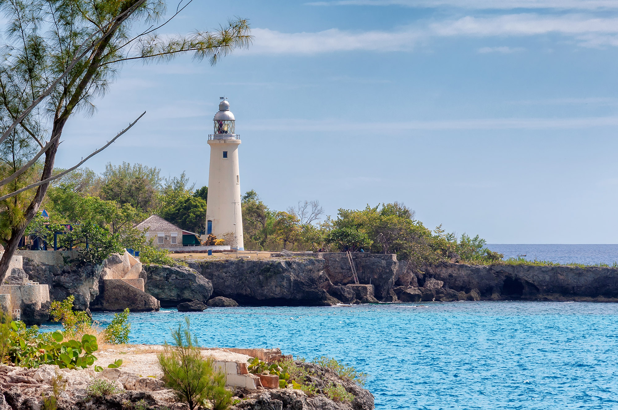 White lighthouse on the coast next to a bright blue coloured sea