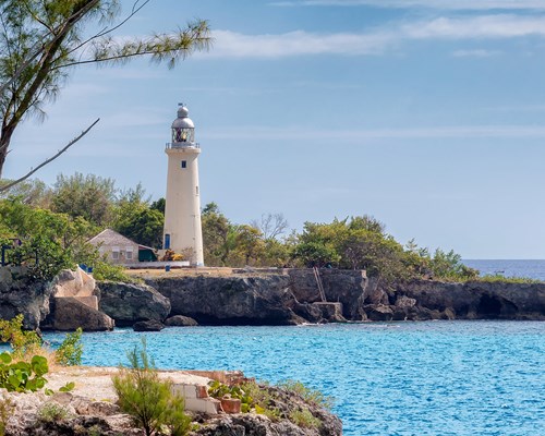 White lighthouse on the coast next to a bright blue coloured sea