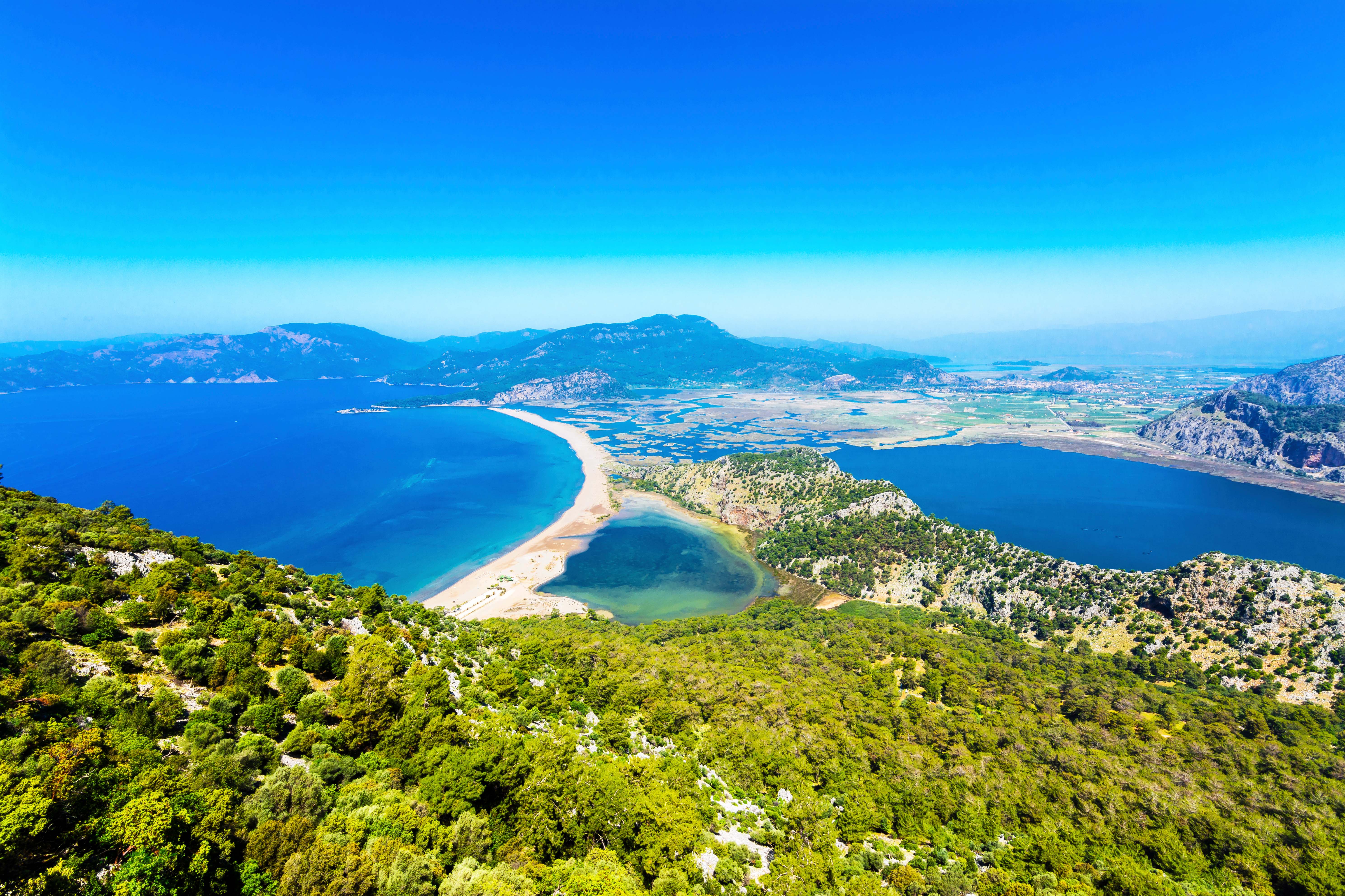 Iztuzu beach near Icmeler with verdant hill in foreground and blue ocean below multi-hued sky
