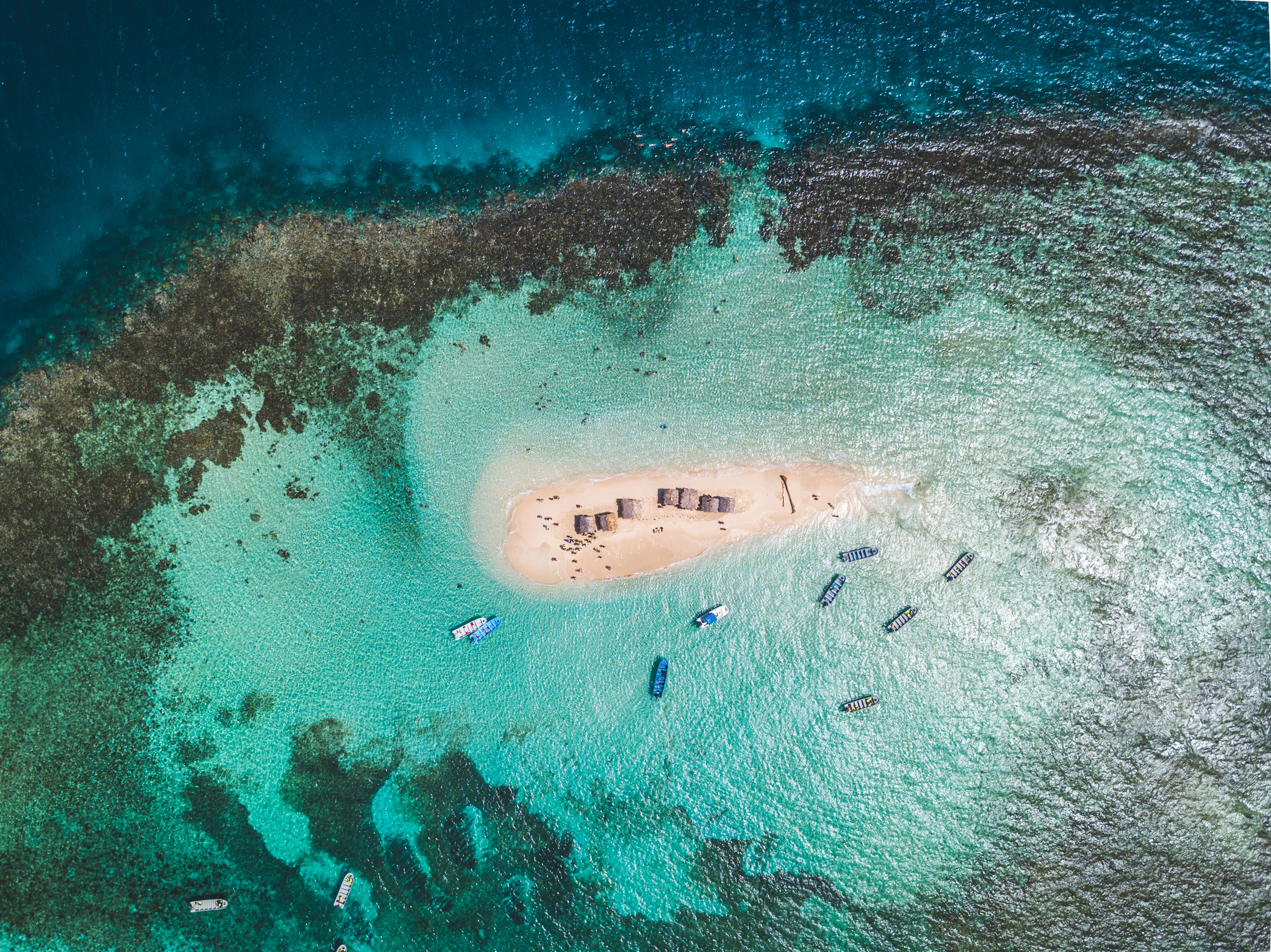 Aerial view of a tiny white sand island with several boats docked near it