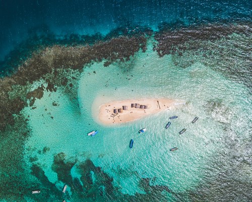 Aerial view of a tiny white sand island with several boats docked near it