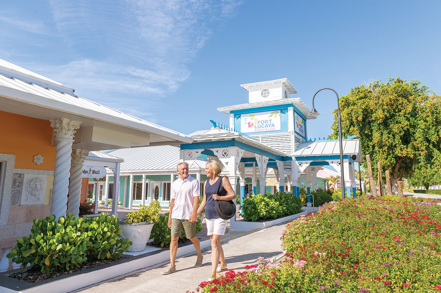 Older couple walking past colourful buildings in Port Lucaya, Freeport