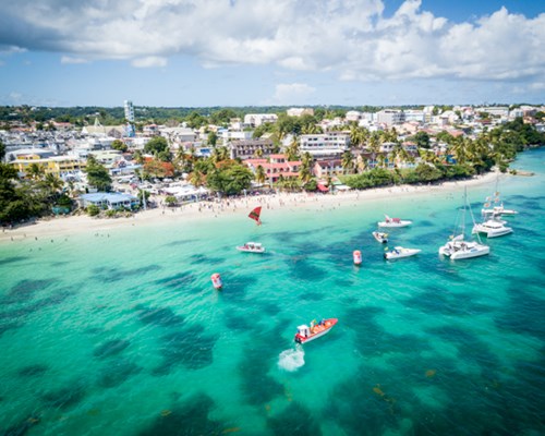 Aerial view of several small boats docked near a tropical white sand beach and town