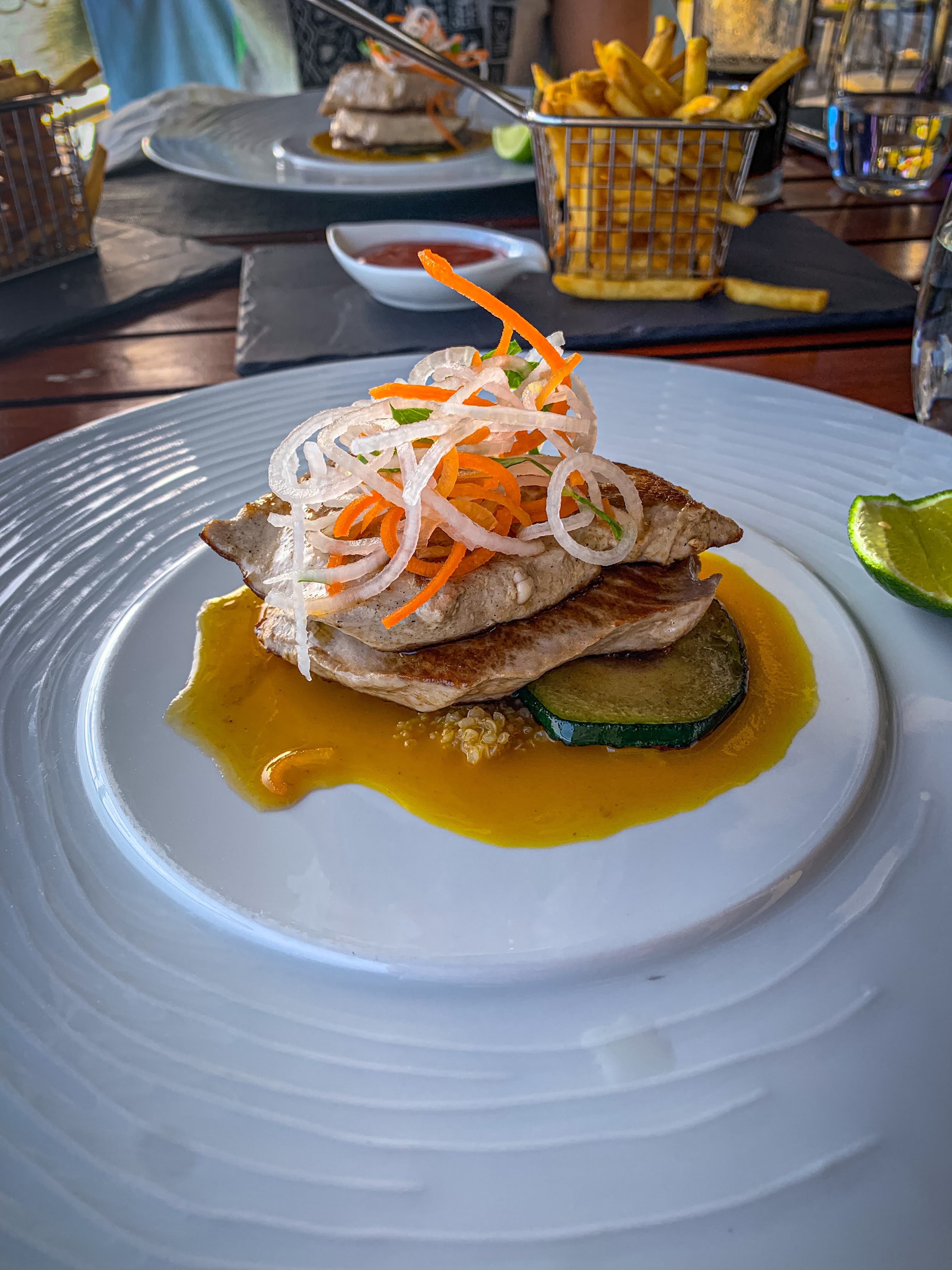 Colourful grilled fish and sliced vegetables on a large white plate on a wooden table
