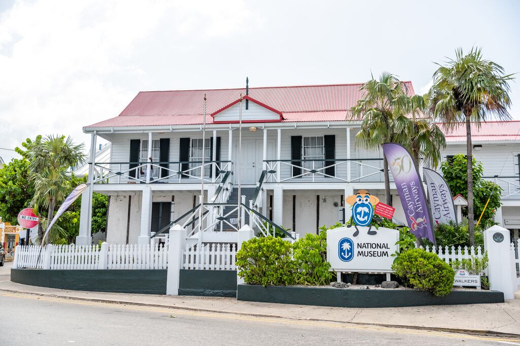 White museum building with red roof next to swaying palm trees - Grand Cayman 