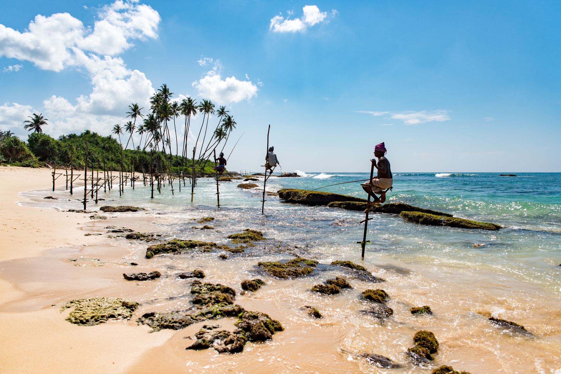 Sri Lanken men standing on sticks with a fishing pole on a wild beach