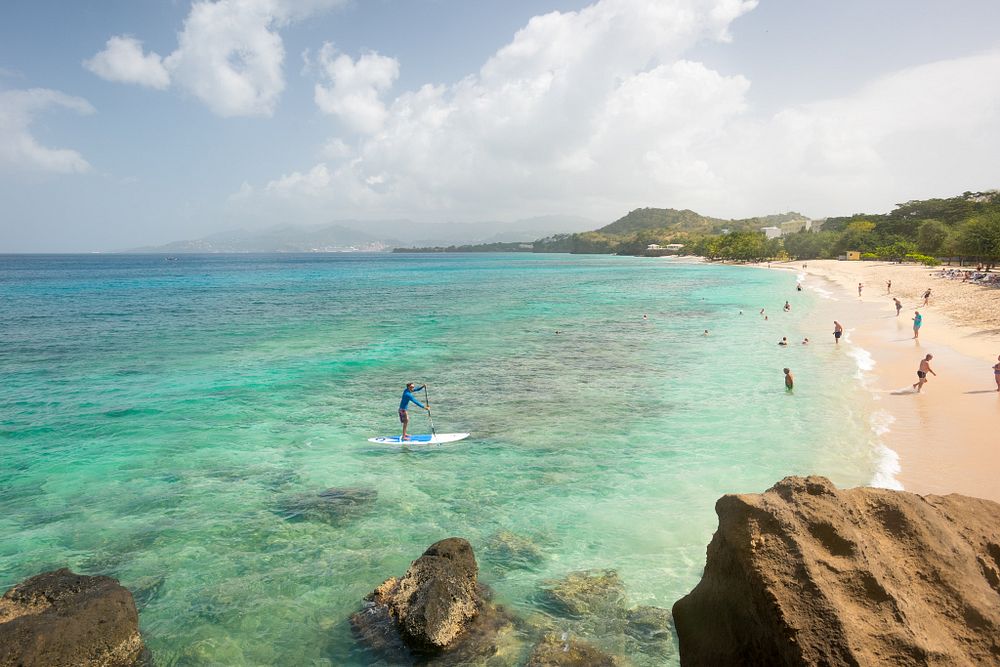 Man paddleboarding in clear tropical sea towards a white sand beach