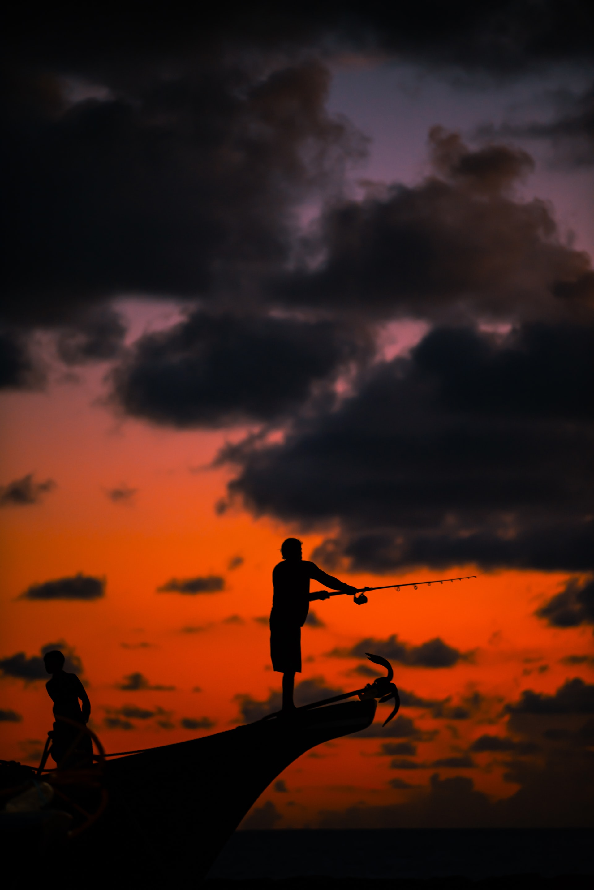 Man Fishing From Front Of Boat With Sunset Sky