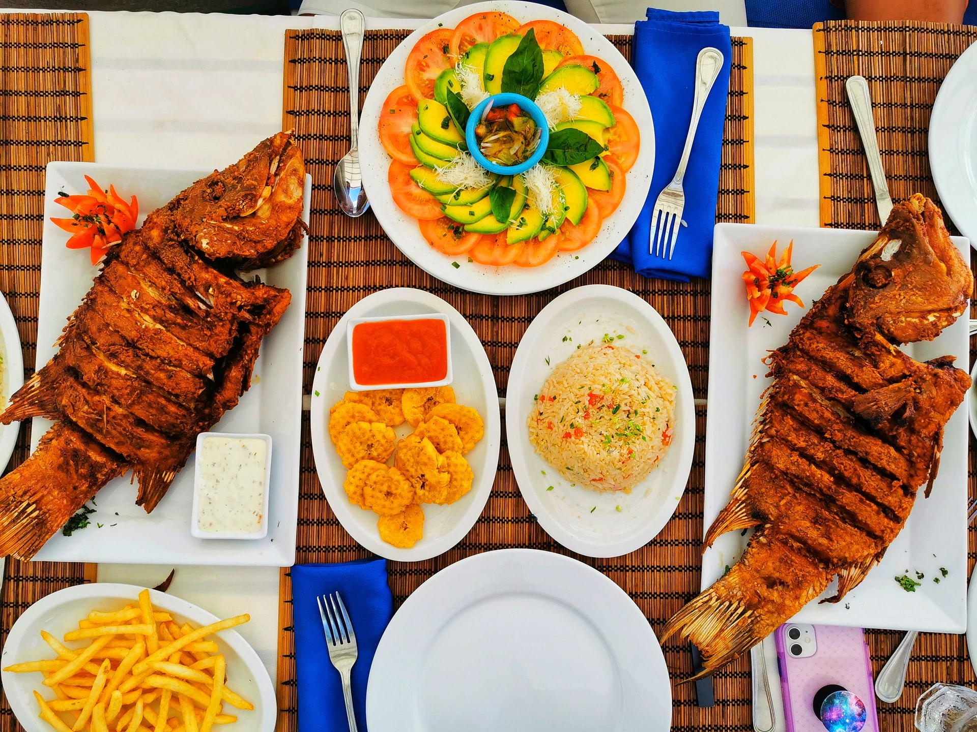 Plates of colourful Caribbean food and fried fish on a wooden table