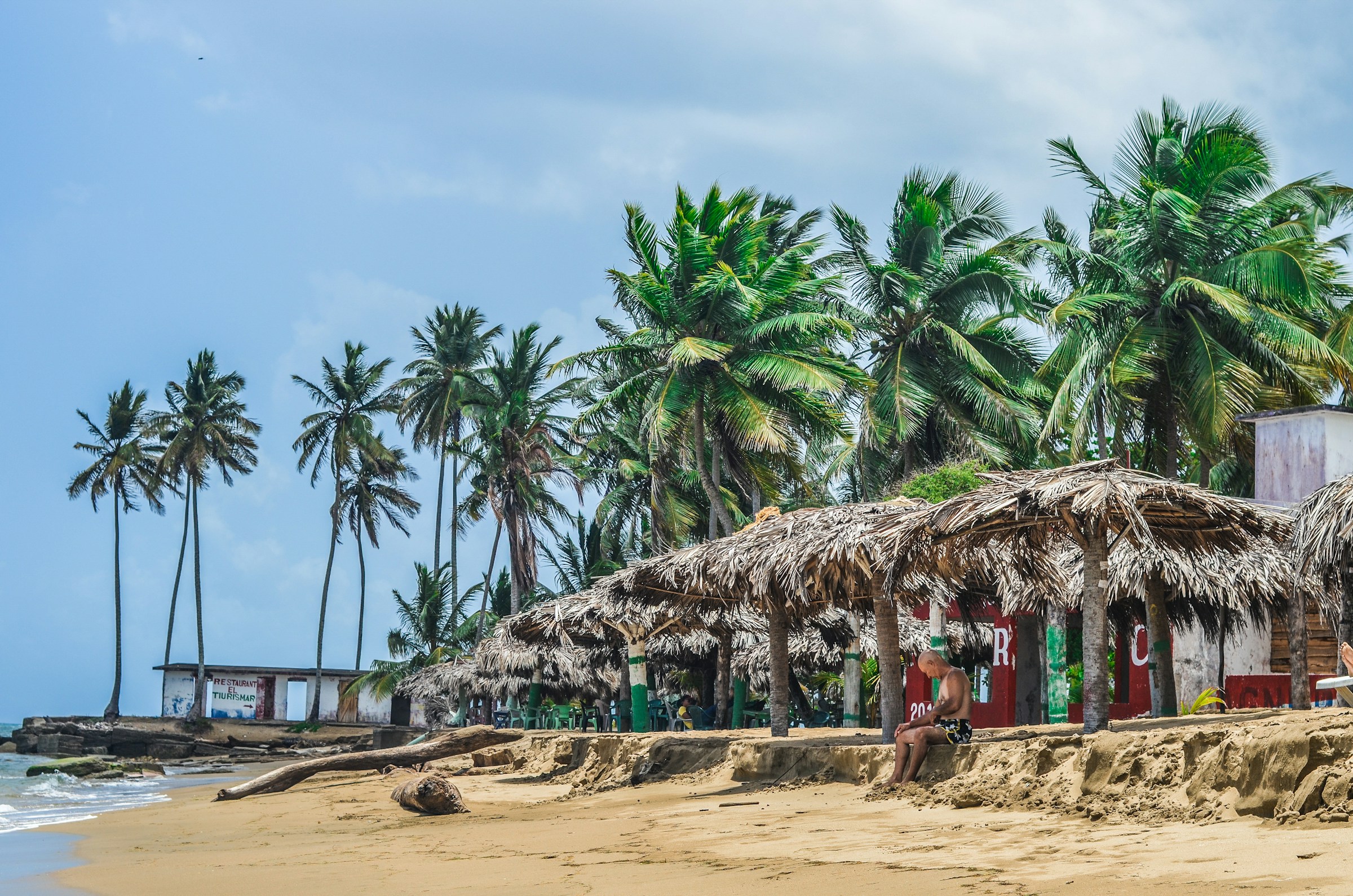 Thatched parasols and beach shacks on a beach fringed by palm trees in Sri Lanka
