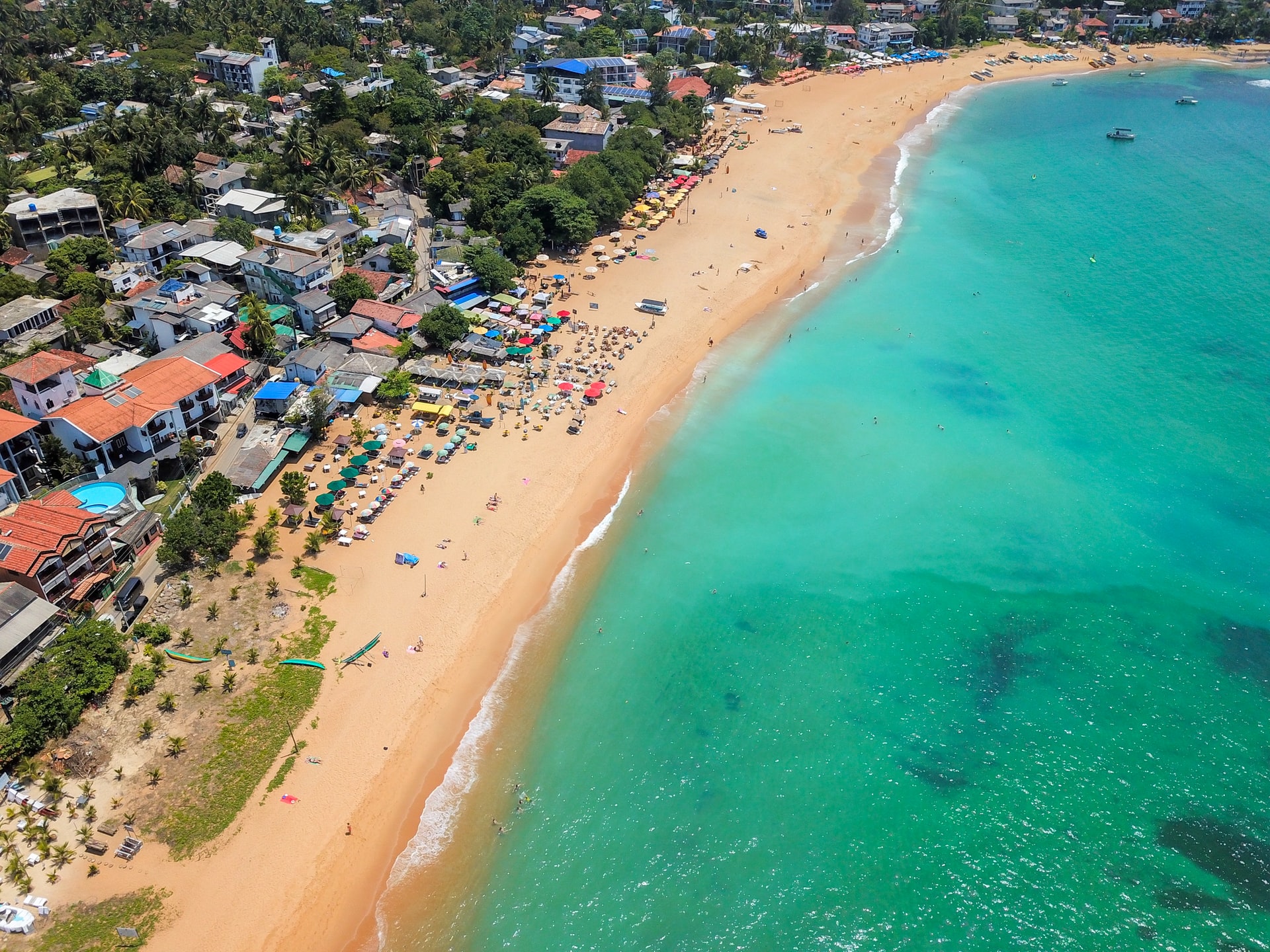 Aerial view of people near the turquoise sea on a tropical beach next to a run down village