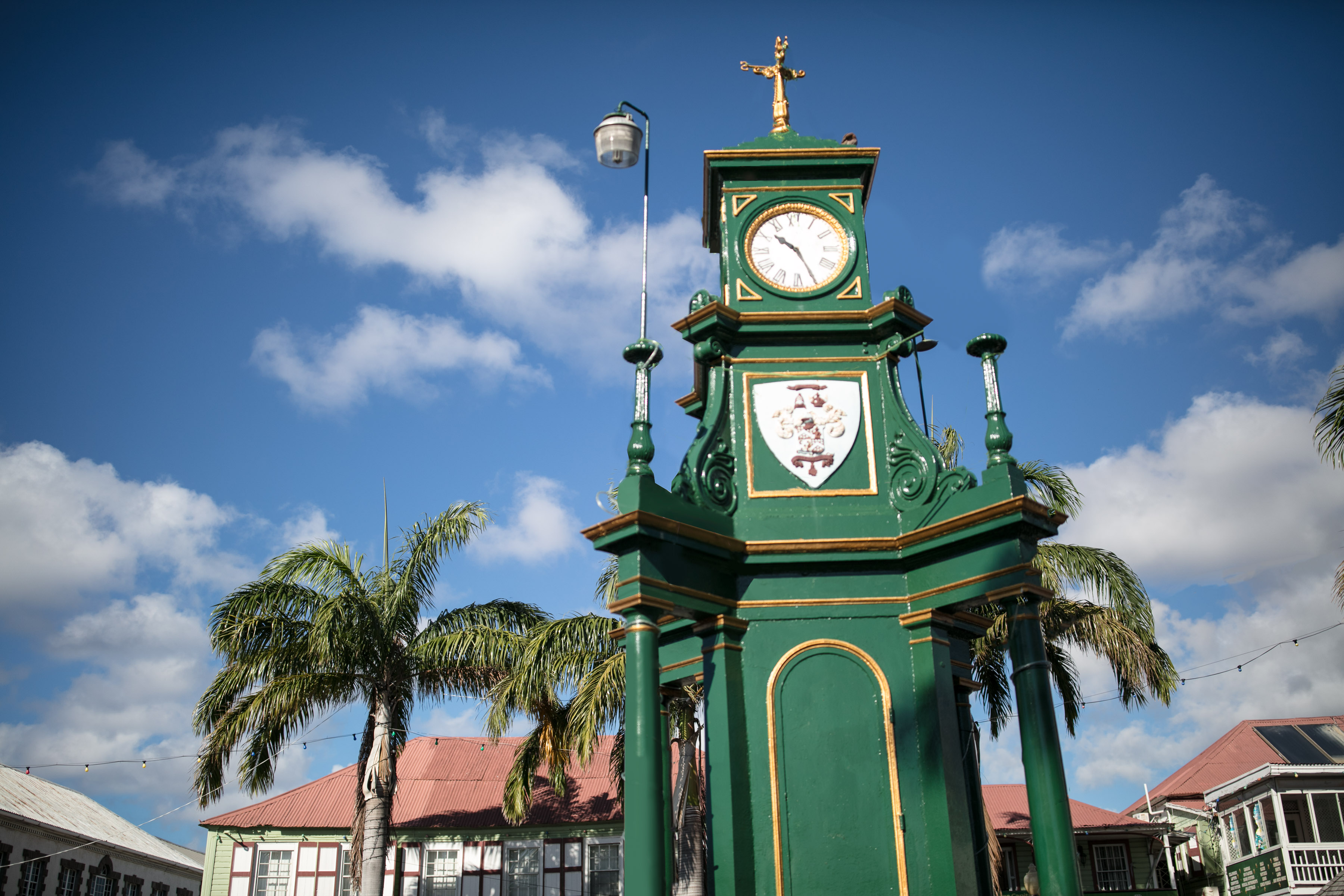 Tall green clock in the middle of a town square on a sunny day