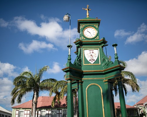Tall green clock in the middle of a town square on a sunny day