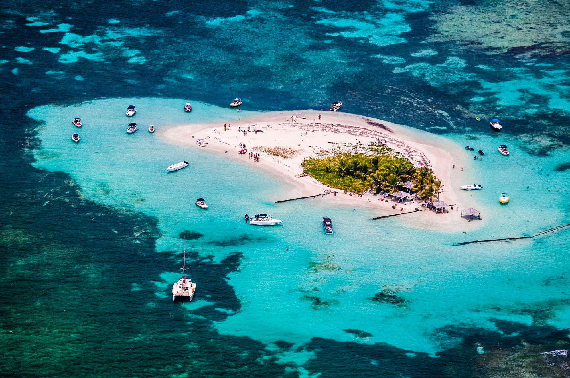 Boats docked around a tiny tropical island with beautiful clear water