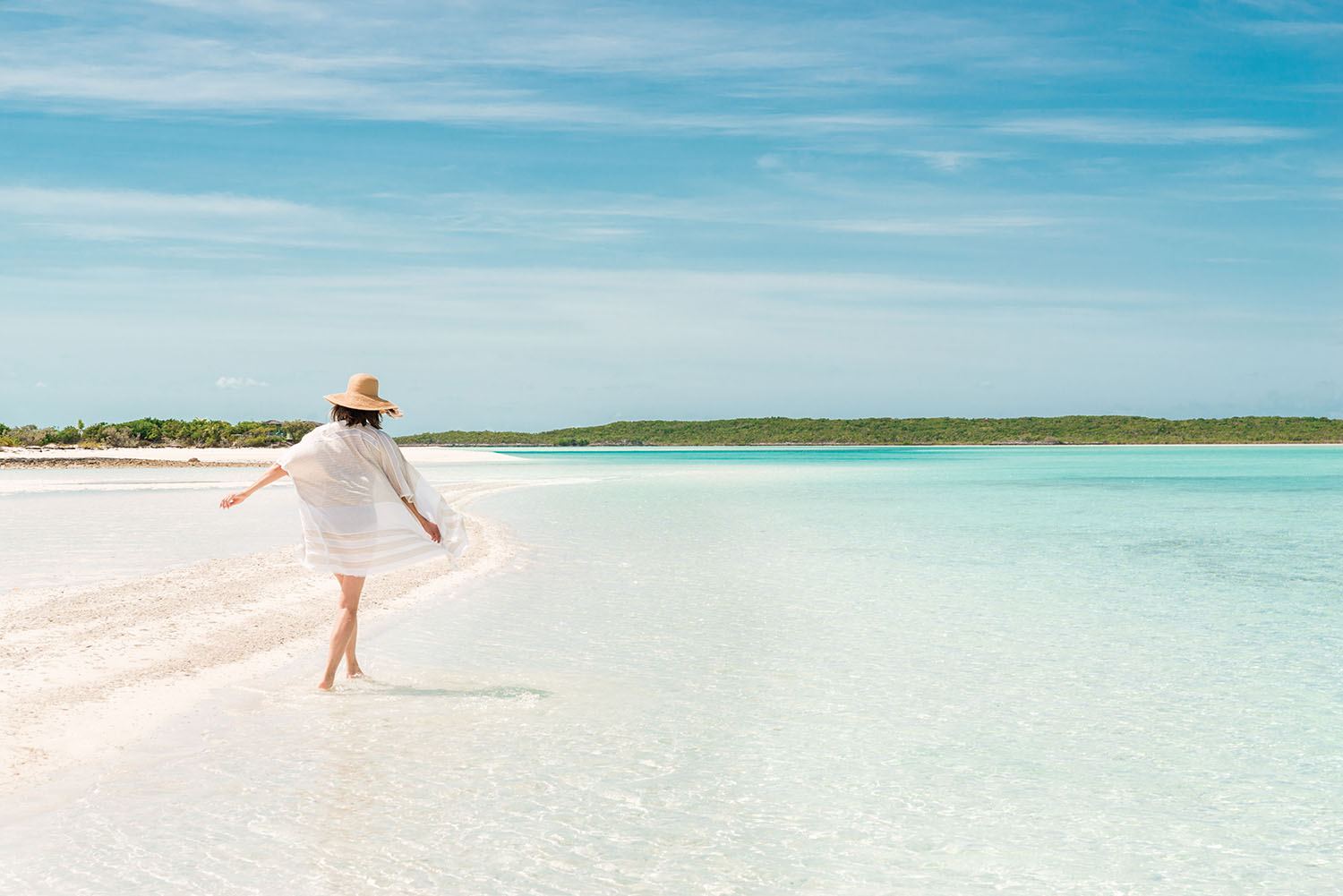 Woman in white dress walking in the shallow water on a tropical beach