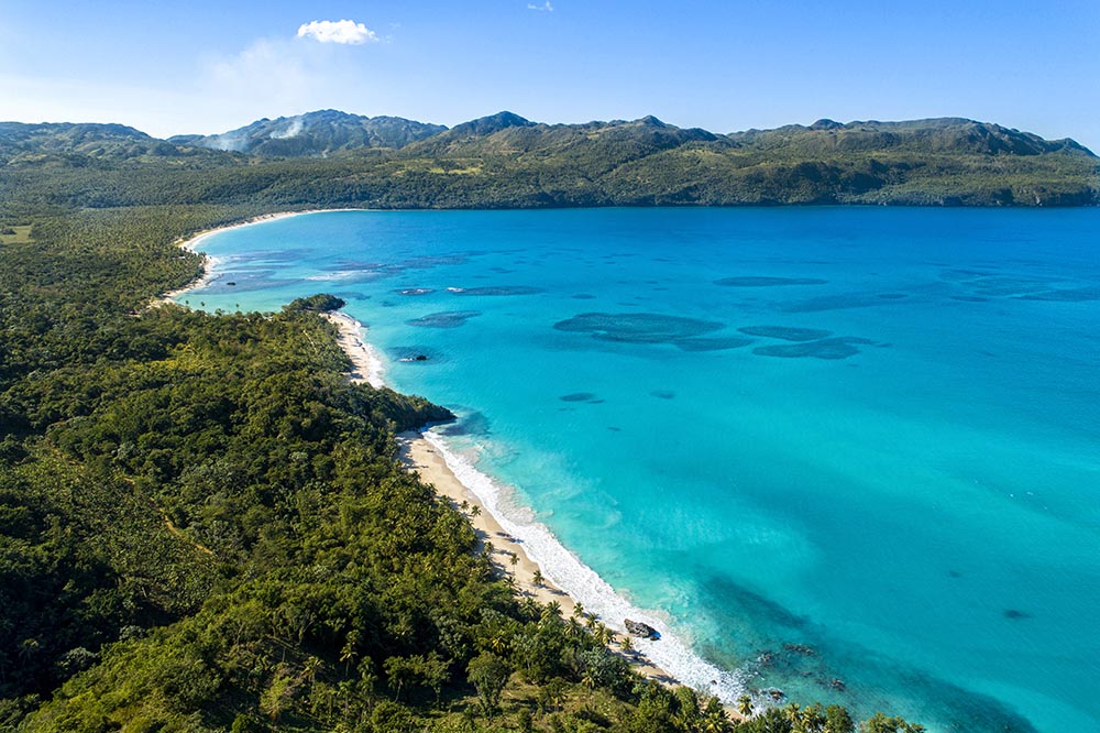 Aerial view of a tropical beach and surrounding forests and mountains 