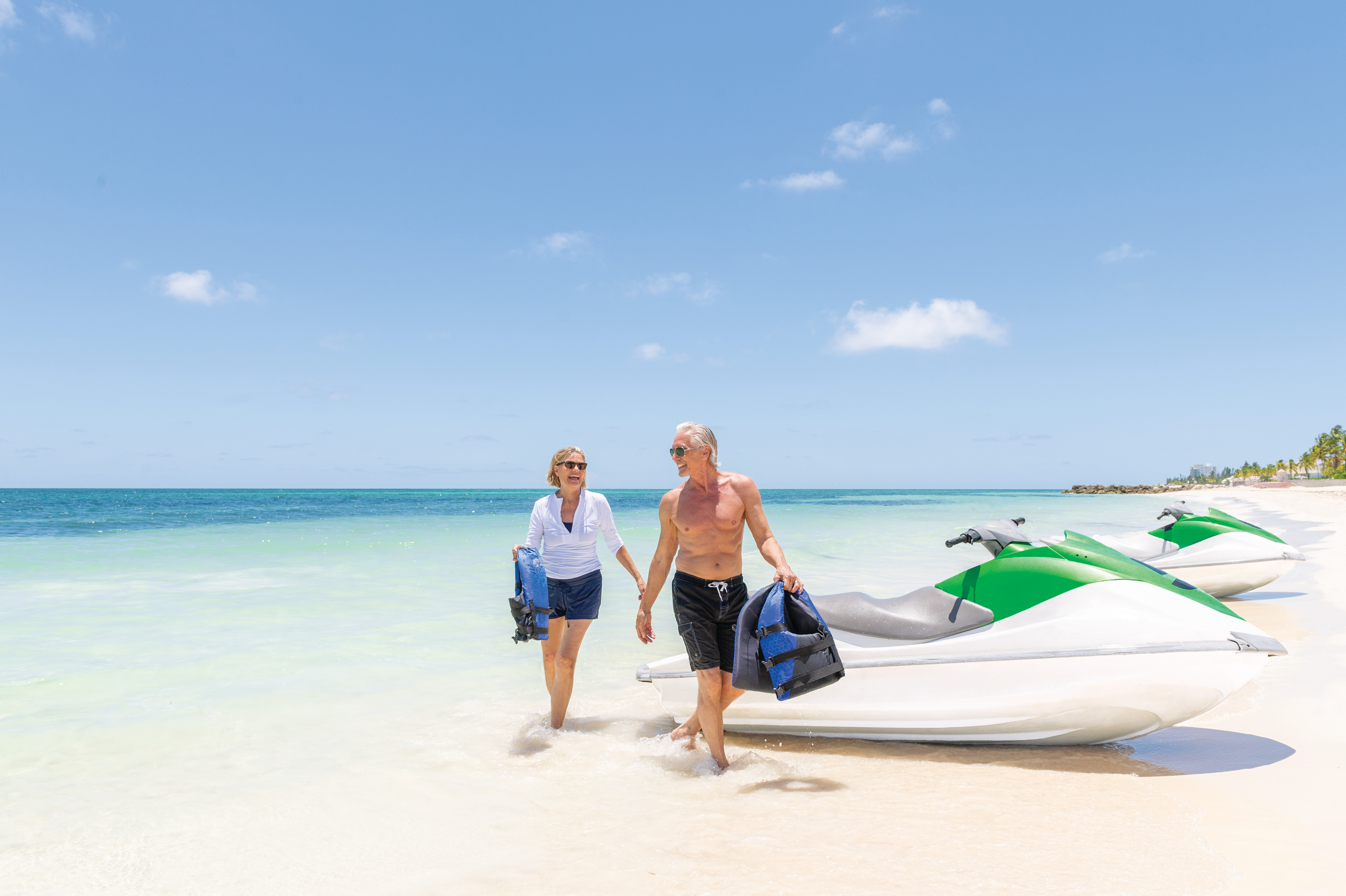 Older couple walking away from jet skis on tropical beach