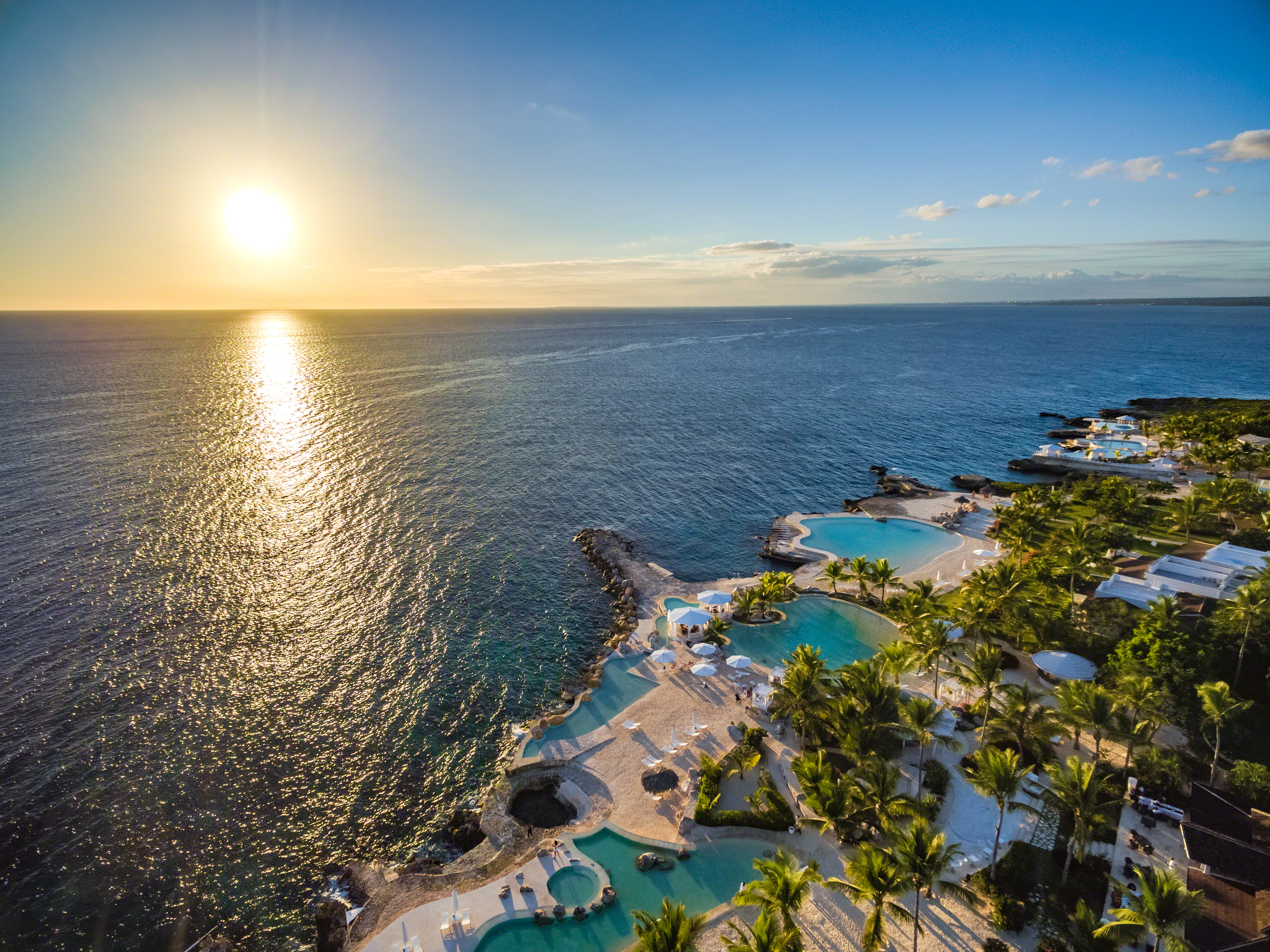 View of a sunset over the sea from a hotel resort with several small pools overlooking the sea