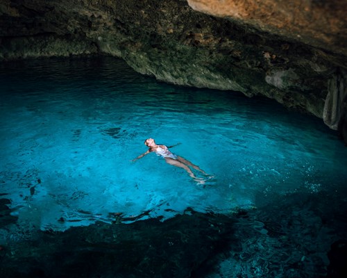 Woman laying in a bright blue pool of water in an underground cave