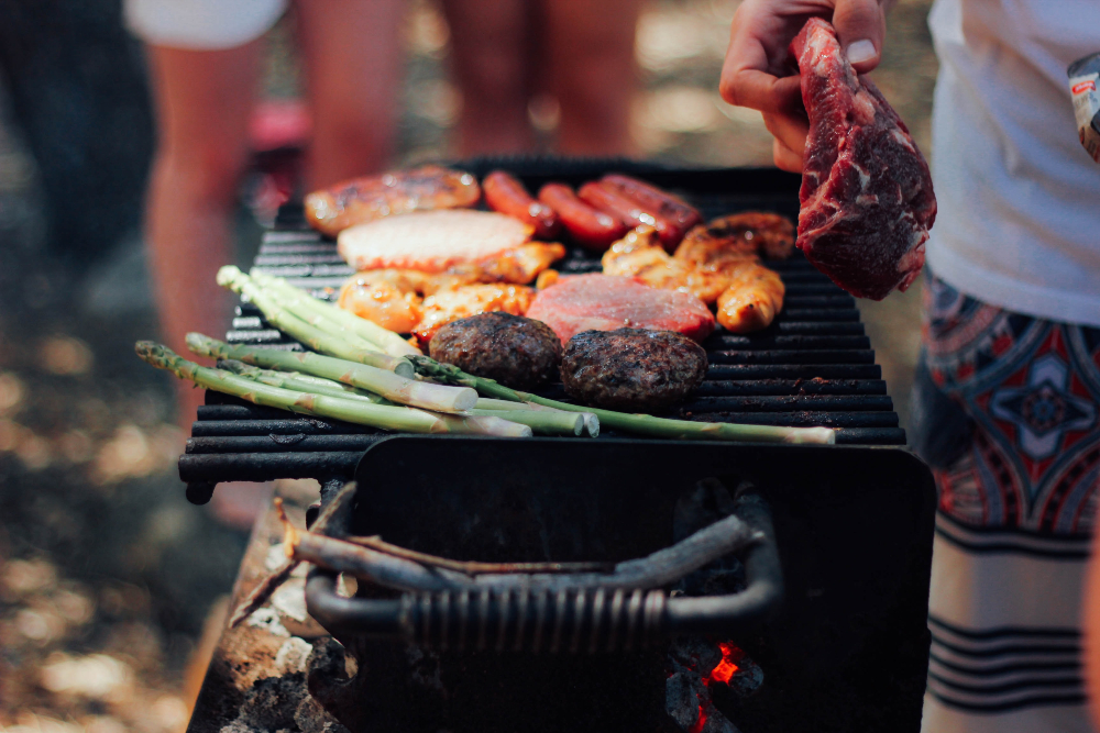 Meat and vegetables grilling on a barbecue with people and sand in the background 