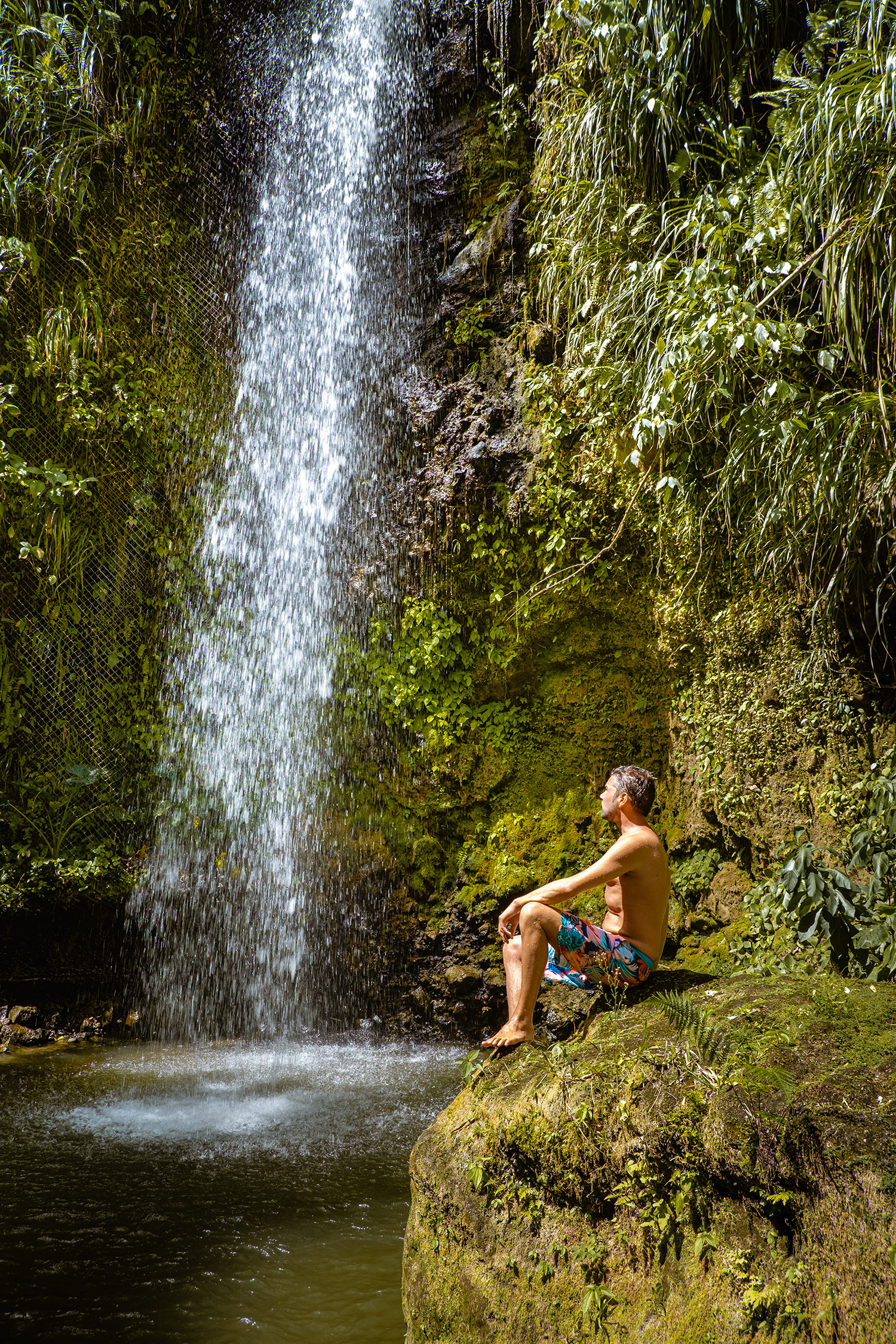 Man posing at bottom of a waterfall in the jungle 