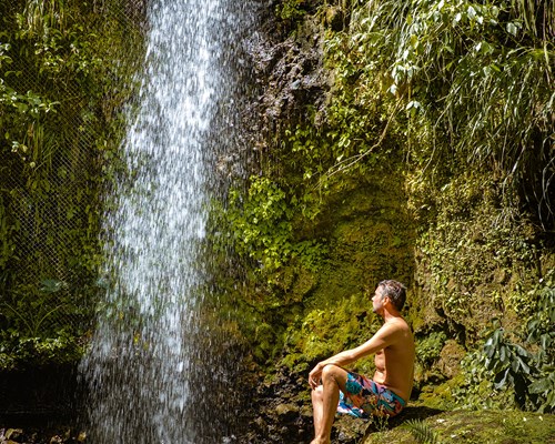 Man posing at bottom of a waterfall in the jungle