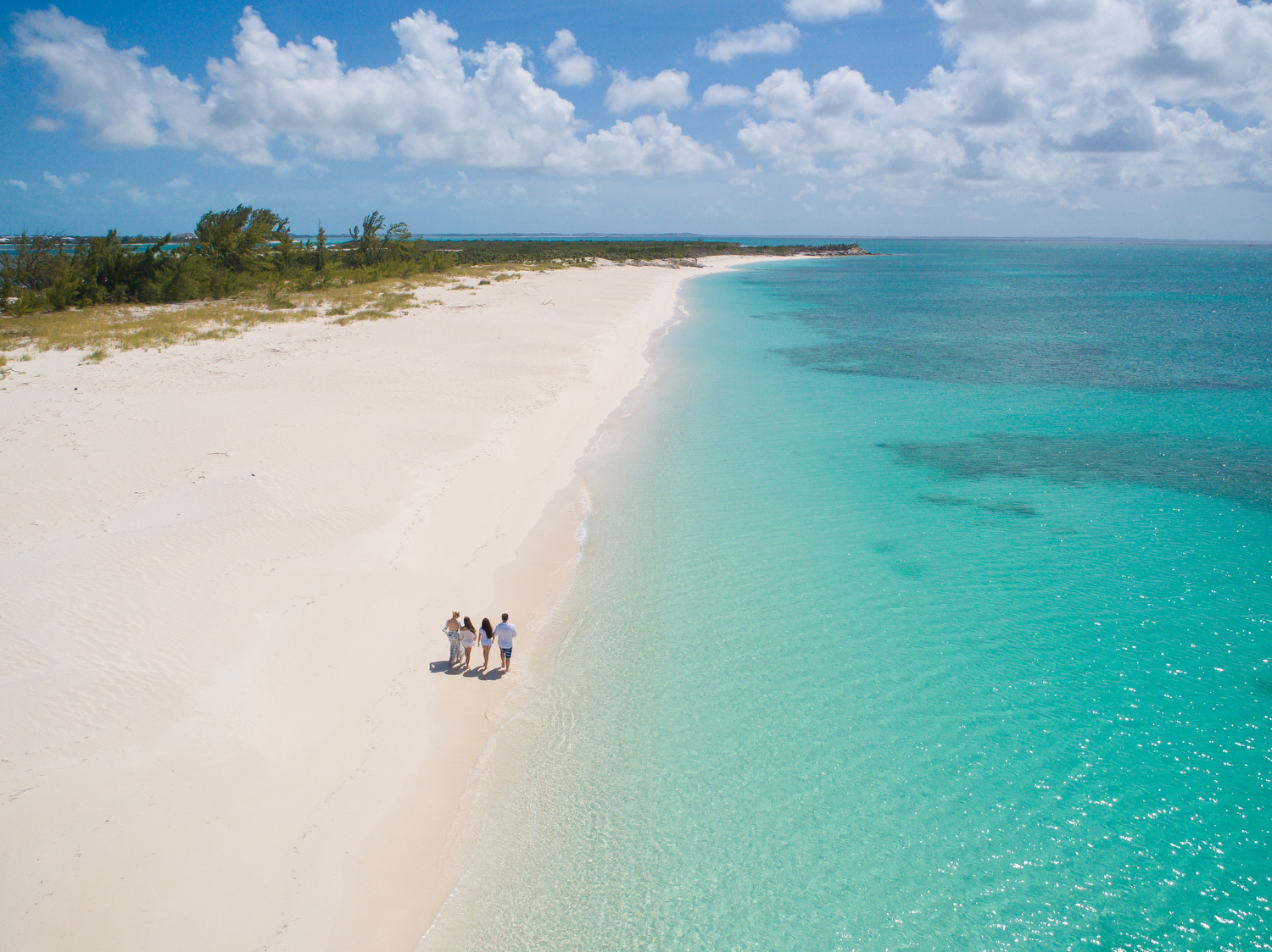 Friends walking down a beautiful tropical beach with white sand and turquoise sea
