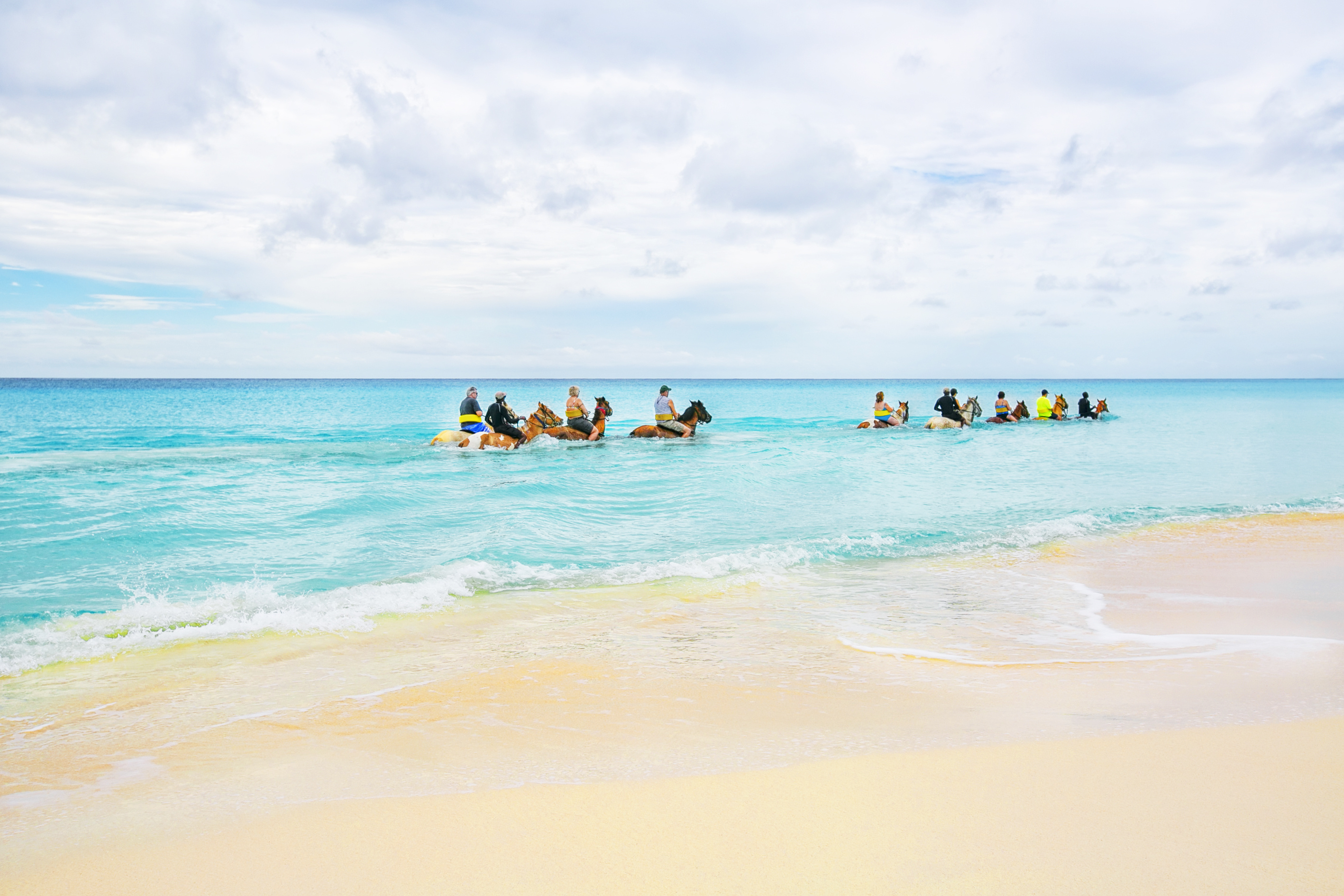 Group of tourists riding horses through a tropical sea