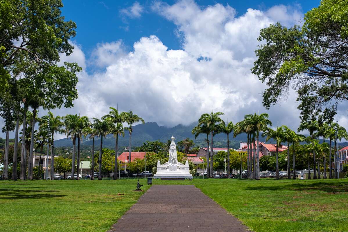 Path leading up to white pointy statue in the middle of a field