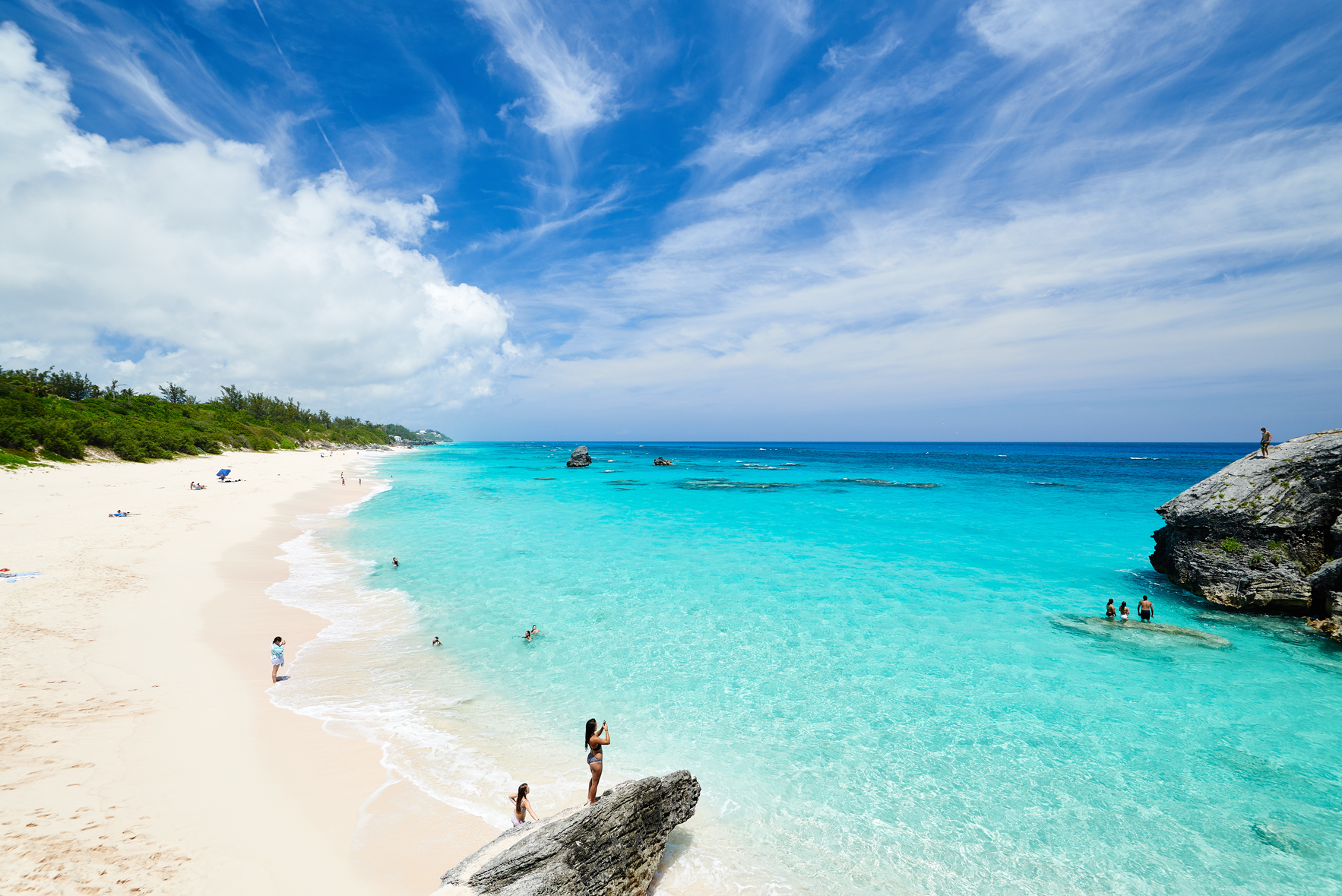 People standing on a rock of a serene white beach with a bluey coast