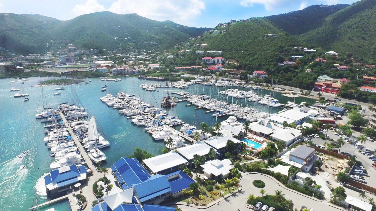 Marina full of boats with colourful buildings and leafy mountains in the background - Soper's Hole, Tortola 
