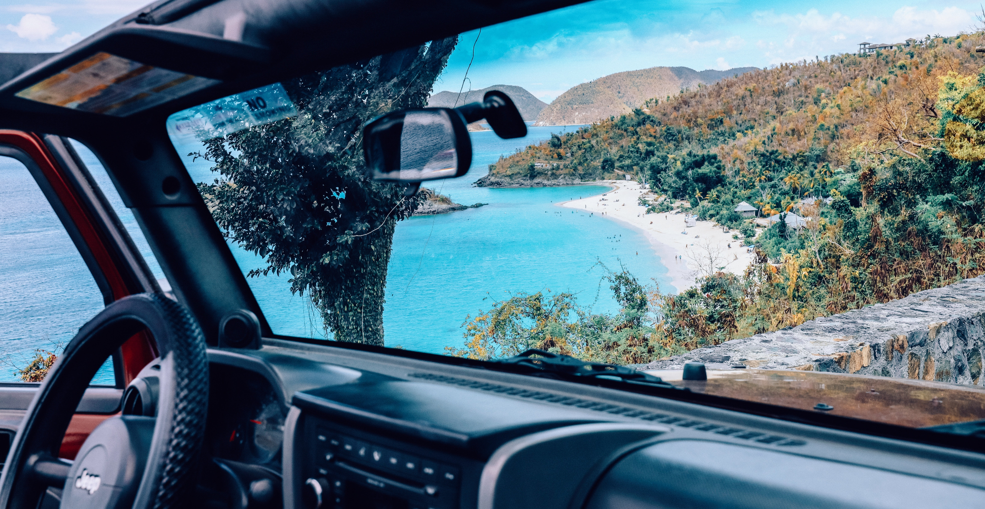 View of sandy beach and leafy mountains through car windscreen - BVI