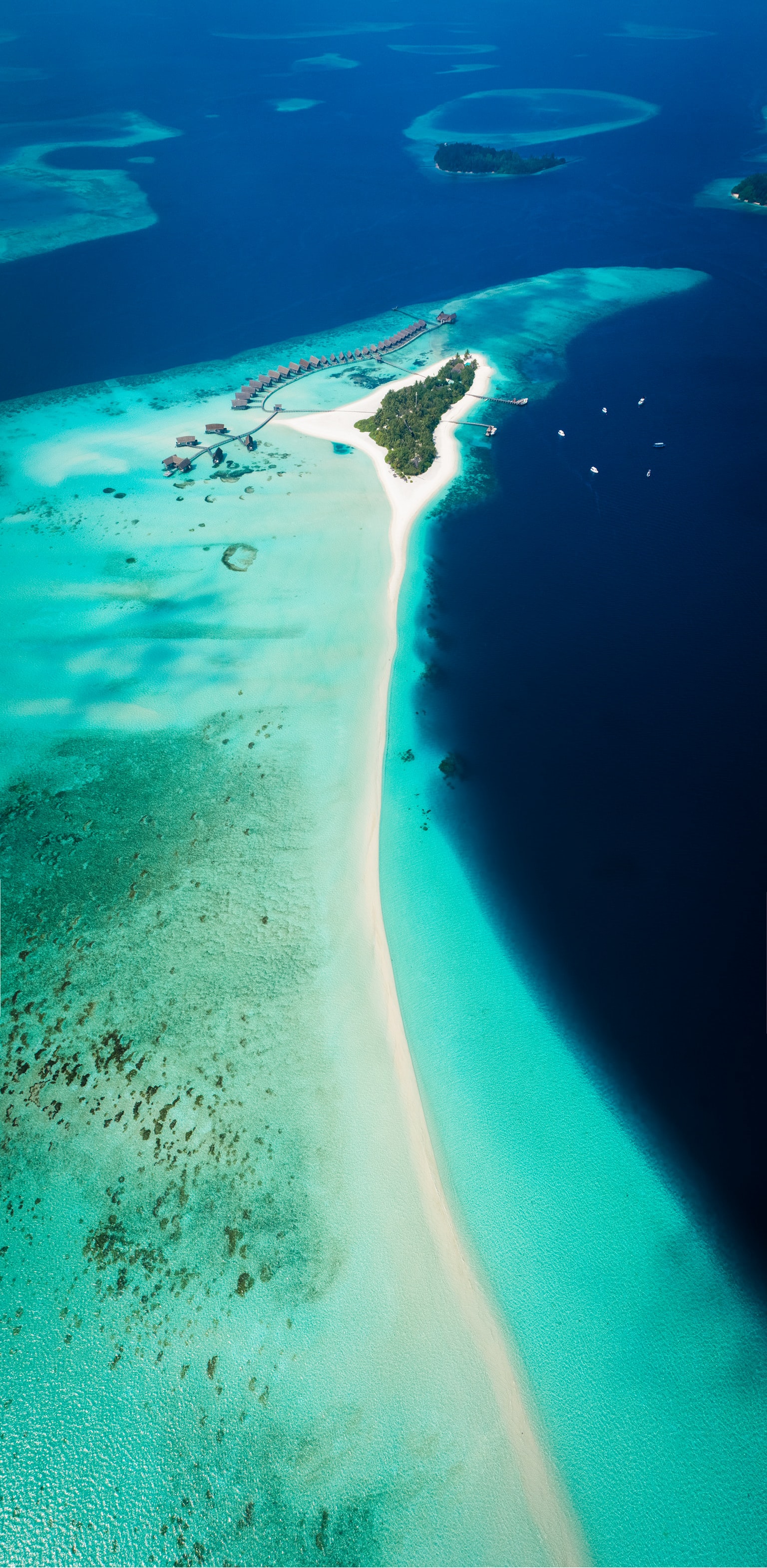 Aerial view of small tropical island resort with bright white sand beach around the outside and shallow blue reefs