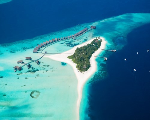Aerial view of small tropical island resort with bright white sand beach around the outside and shallow blue reefs