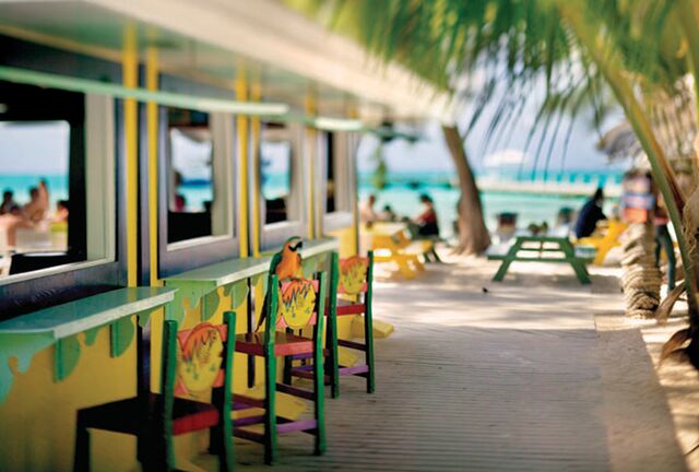 Colourful beach bar and chairs with a busy beach and palm trees in the background - Rum Point, Cayman islands