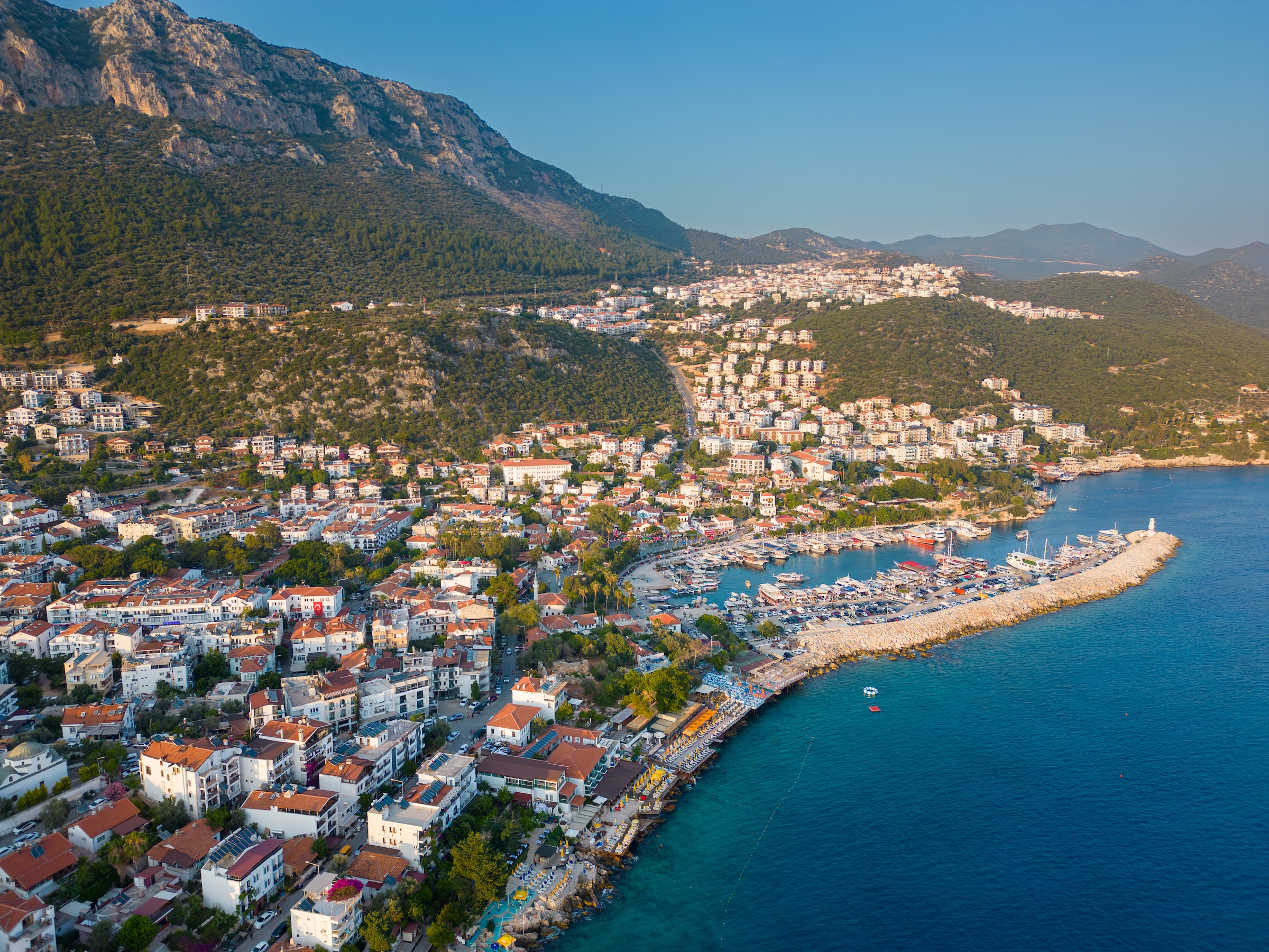 An aerial view of a town harbour by the sea backed by mountainous terrain 