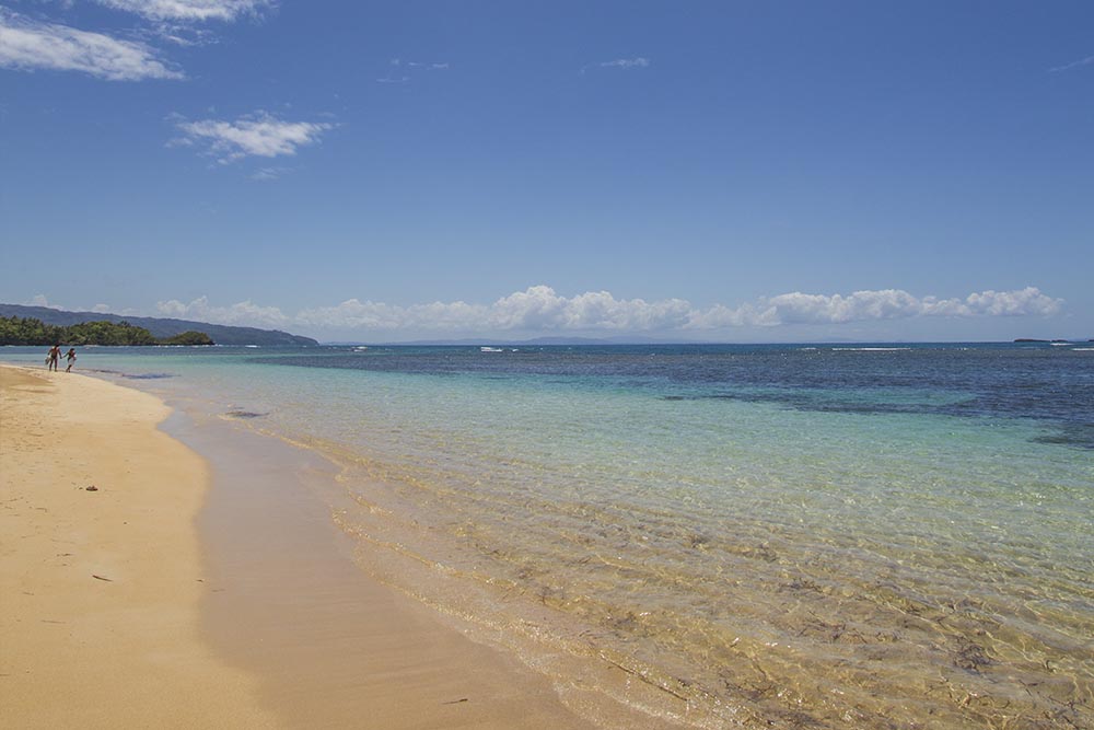 2 people walking along a golden sand beach with clear turquoise waters