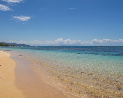 2 people walking along a golden sand beach with clear turquoise waters